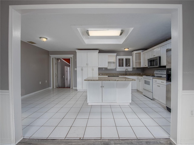 kitchen with light stone countertops, white cabinets, white electric range, a kitchen island, and light tile patterned flooring