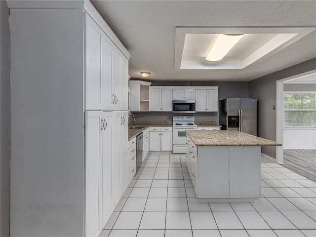 kitchen featuring a raised ceiling, sink, light stone countertops, a kitchen island, and stainless steel appliances