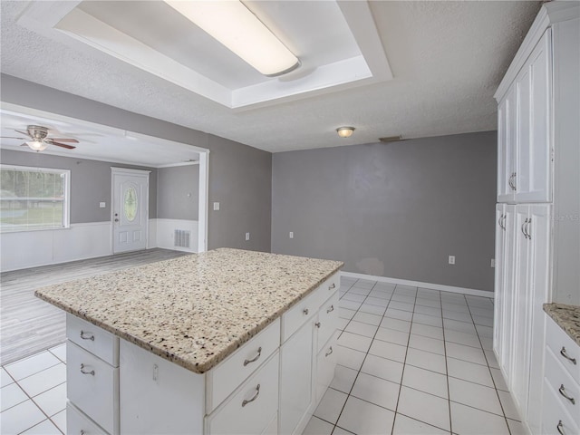 kitchen featuring white cabinets, a kitchen island, a raised ceiling, and light tile patterned floors