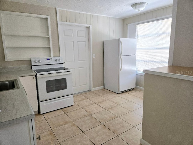 kitchen featuring wood walls, sink, light tile patterned floors, white appliances, and a textured ceiling