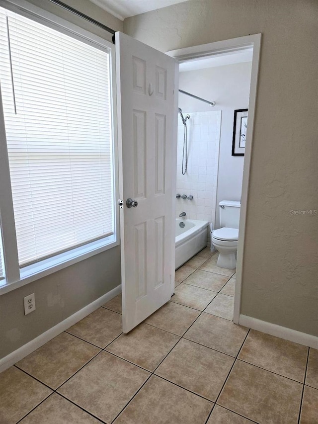 bathroom featuring toilet, tiled shower / bath combo, and tile patterned flooring