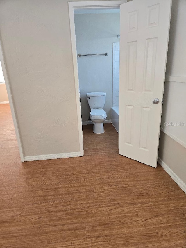 bathroom with wood-type flooring, a tub, and toilet