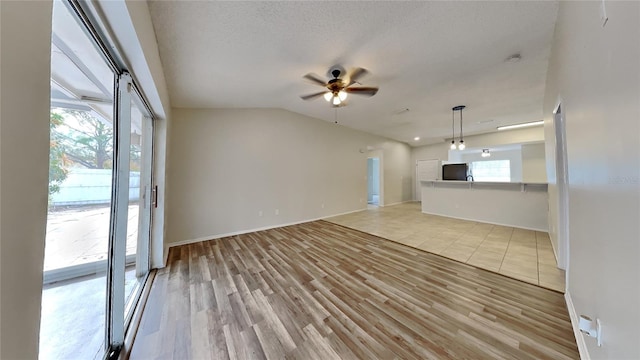 unfurnished living room with ceiling fan, lofted ceiling, a textured ceiling, and light hardwood / wood-style flooring