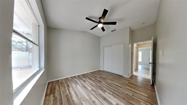 unfurnished bedroom featuring vaulted ceiling, ceiling fan, light wood-type flooring, a textured ceiling, and a closet