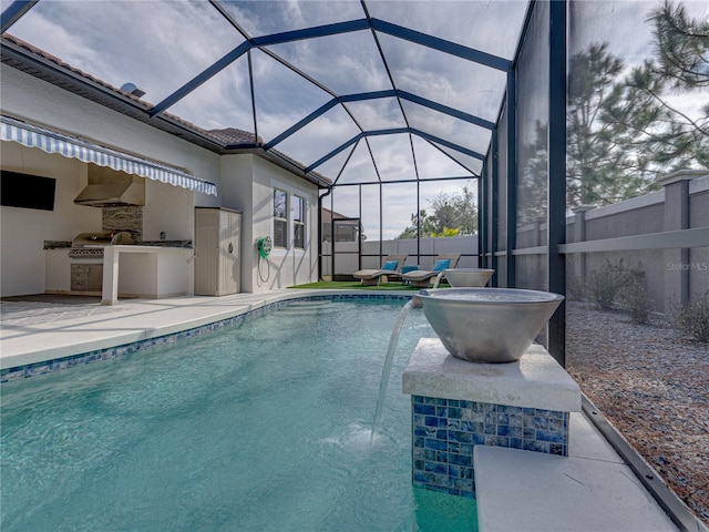 view of swimming pool featuring a patio, a lanai, pool water feature, area for grilling, and exterior kitchen