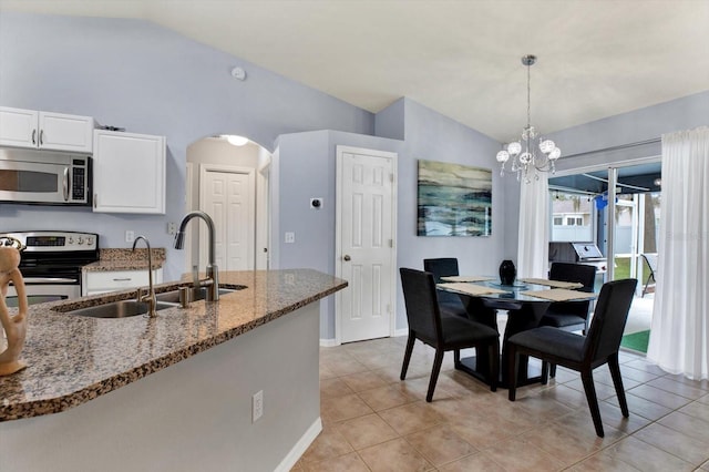 kitchen with stainless steel appliances, dark stone countertops, hanging light fixtures, vaulted ceiling, and white cabinets