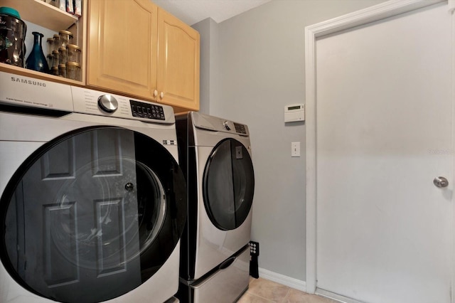 clothes washing area featuring washing machine and dryer, light tile patterned flooring, and cabinets