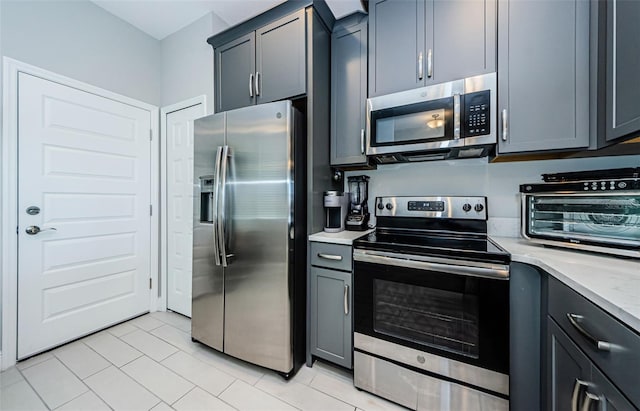 kitchen with gray cabinetry, light stone counters, light tile patterned floors, and stainless steel appliances