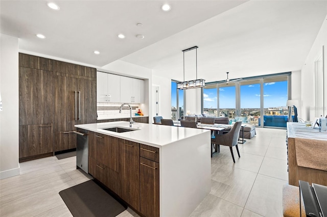 kitchen featuring pendant lighting, white cabinetry, expansive windows, sink, and a center island with sink