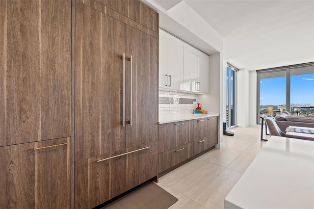 kitchen featuring decorative backsplash, white cabinetry, light tile patterned floors, and expansive windows