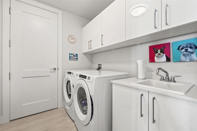 clothes washing area with washer and clothes dryer, sink, light hardwood / wood-style floors, and cabinets