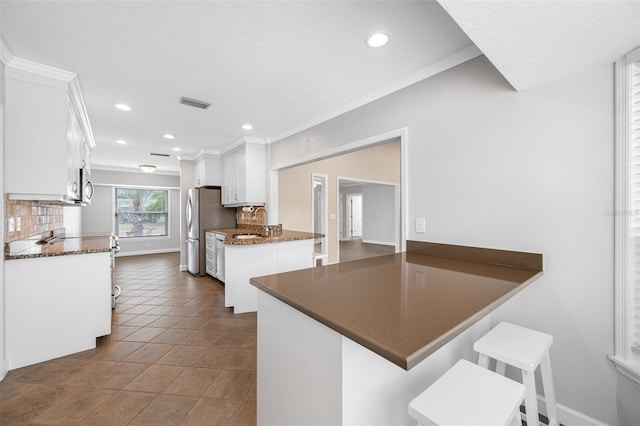 kitchen with kitchen peninsula, dark tile patterned flooring, crown molding, white cabinetry, and a kitchen breakfast bar