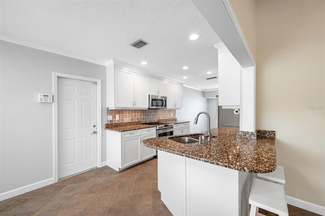 kitchen with sink, white cabinets, dark stone countertops, kitchen peninsula, and appliances with stainless steel finishes