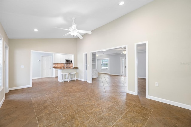 unfurnished living room with ceiling fan, high vaulted ceiling, and tile patterned floors