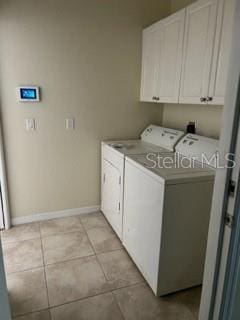 clothes washing area with cabinets, washer and clothes dryer, and light tile patterned floors