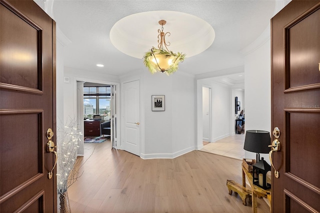 entryway with a tray ceiling, light hardwood / wood-style floors, and ornamental molding