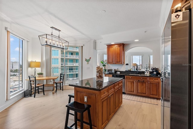 kitchen featuring pendant lighting, light hardwood / wood-style floors, ornamental molding, a kitchen island, and stainless steel appliances