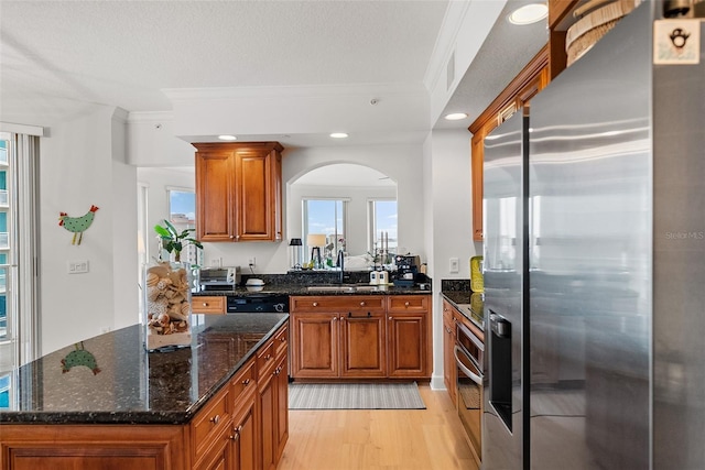 kitchen with dark stone counters, crown molding, sink, light wood-type flooring, and appliances with stainless steel finishes