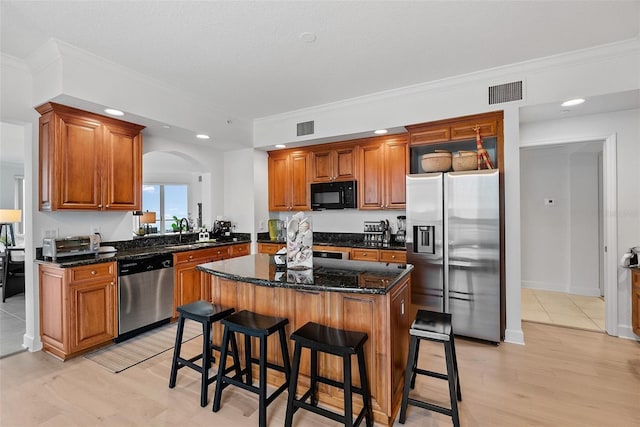 kitchen with a center island, sink, stainless steel appliances, dark stone counters, and a breakfast bar