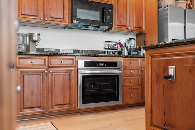 kitchen with stainless steel oven, dark stone counters, and light hardwood / wood-style flooring