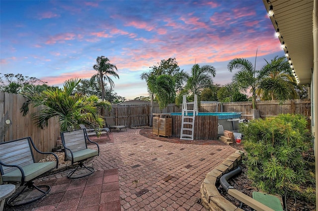 patio terrace at dusk featuring a fenced in pool