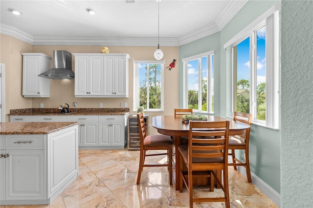 kitchen with crown molding, white cabinetry, stone countertops, decorative light fixtures, and wall chimney exhaust hood