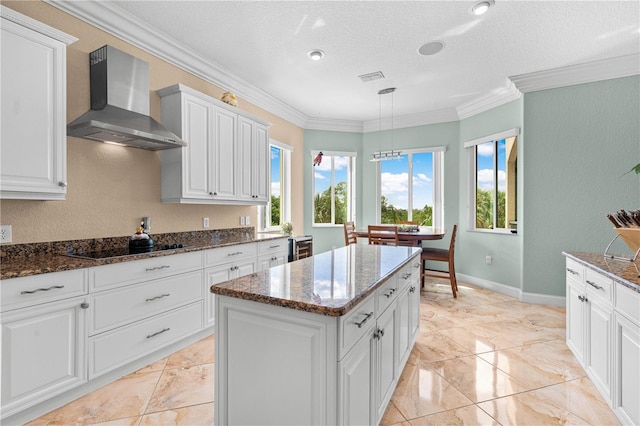 kitchen featuring a center island, wall chimney range hood, pendant lighting, dark stone counters, and white cabinets