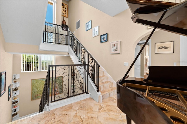 stairs featuring visible vents, arched walkways, marble finish floor, and a high ceiling