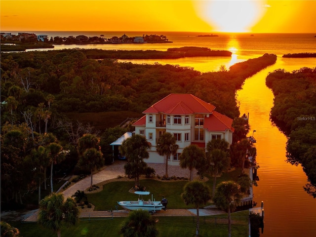 aerial view at dusk with a water view and a wooded view