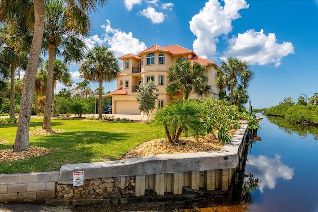 mediterranean / spanish home featuring an attached garage, stucco siding, a front yard, a water view, and a balcony