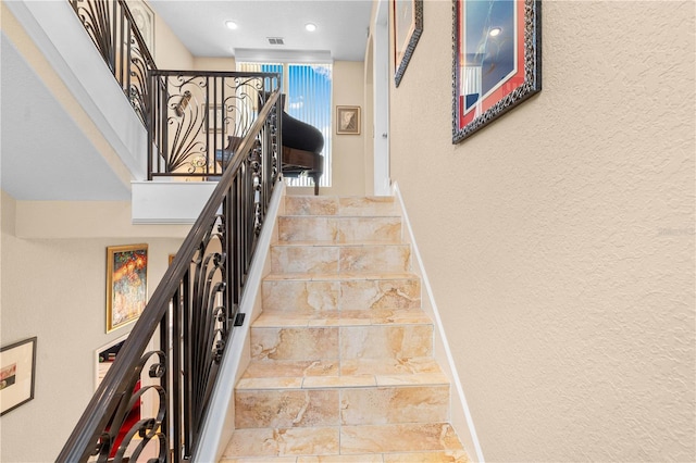 staircase with stone finish flooring, visible vents, baseboards, a textured wall, and recessed lighting