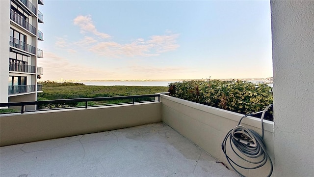 balcony at dusk featuring a water view