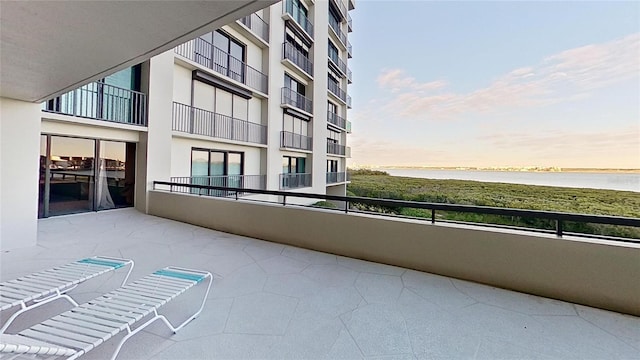 balcony at dusk featuring a water view