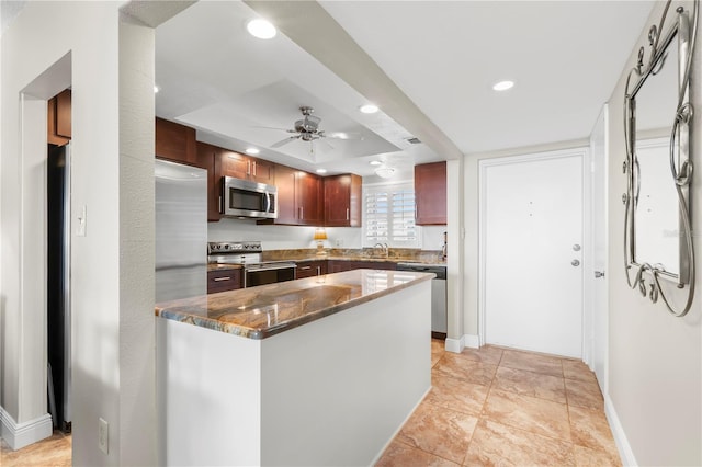 kitchen featuring dark stone countertops, appliances with stainless steel finishes, ceiling fan, a tray ceiling, and sink