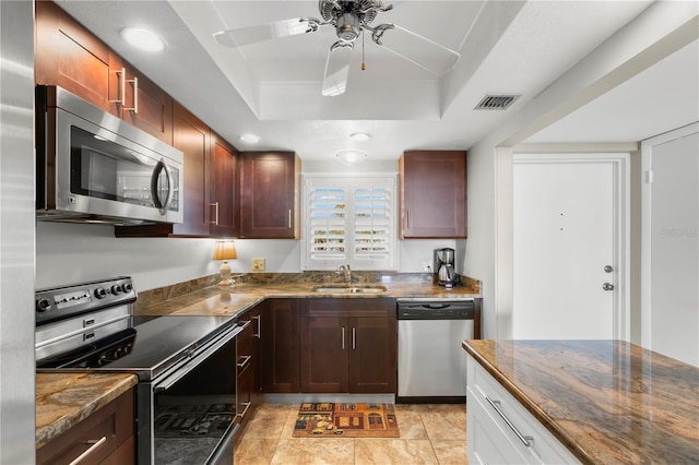 kitchen with sink, dark stone countertops, ceiling fan, a tray ceiling, and appliances with stainless steel finishes