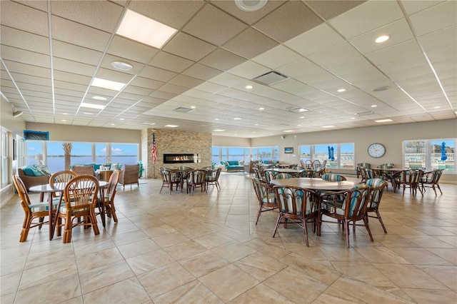 dining space featuring a healthy amount of sunlight, a paneled ceiling, and a stone fireplace