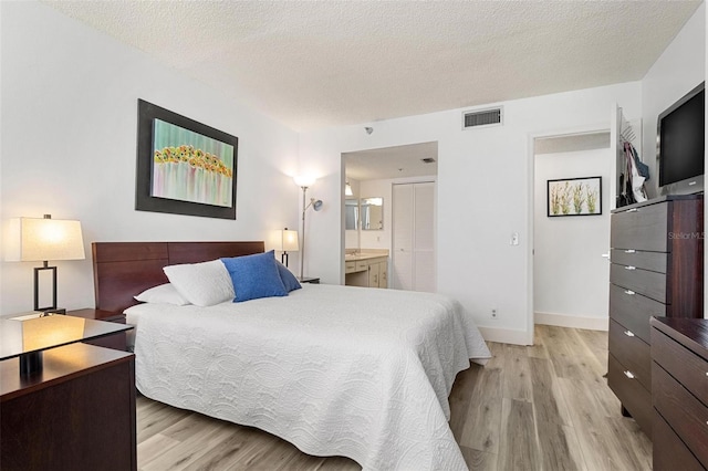 bedroom featuring light hardwood / wood-style floors, a textured ceiling, and ensuite bathroom