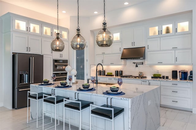 kitchen with a center island with sink, light stone countertops, white cabinetry, and high end refrigerator