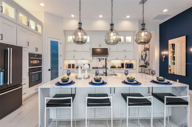 kitchen with light stone countertops, backsplash, high quality fridge, and a large island