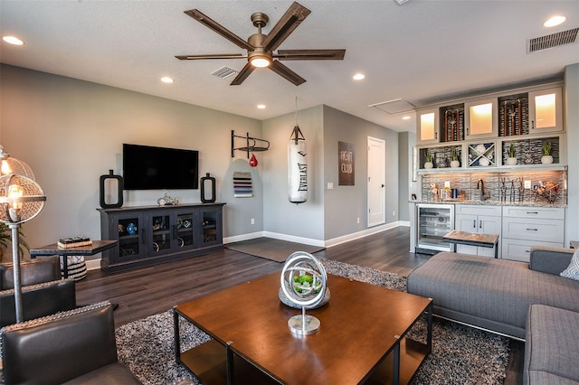 living room featuring ceiling fan, beverage cooler, dark hardwood / wood-style flooring, indoor wet bar, and a textured ceiling