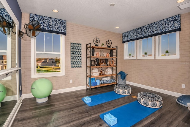 workout area with dark wood-type flooring, brick wall, and a textured ceiling