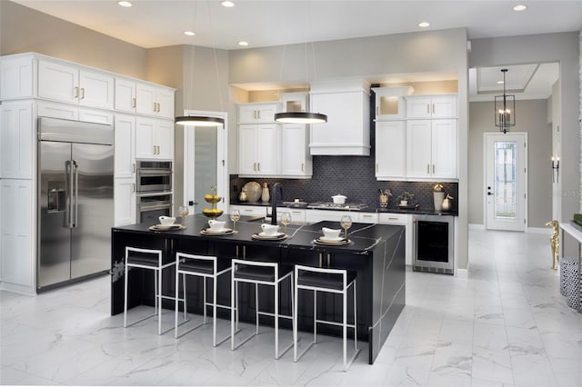 kitchen with tasteful backsplash, wine cooler, white cabinets, stainless steel appliances, and a center island with sink