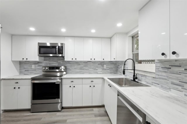 kitchen with stainless steel appliances, decorative backsplash, white cabinetry, and sink