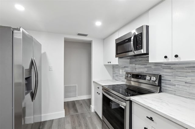 kitchen featuring decorative backsplash, white cabinets, appliances with stainless steel finishes, and light hardwood / wood-style flooring