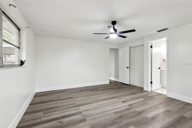 unfurnished bedroom with ensuite bath, a ceiling fan, baseboards, wood finished floors, and visible vents
