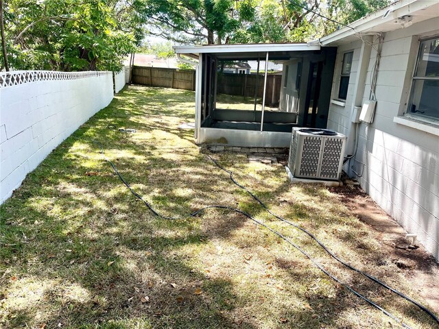 view of yard featuring a fenced backyard, a sunroom, and central AC