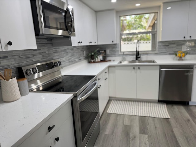 kitchen with white cabinets, a sink, light wood-style flooring, stainless steel appliances, and tasteful backsplash