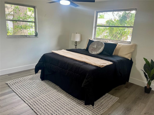bedroom with baseboards, ceiling fan, wood finished floors, and multiple windows