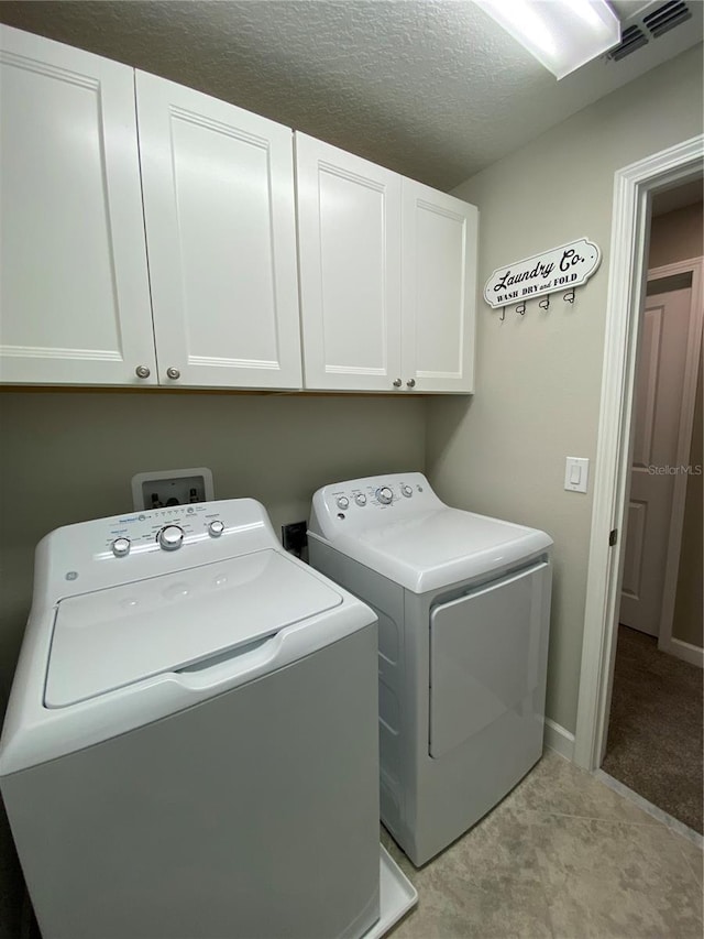 laundry area featuring cabinets, washing machine and clothes dryer, and a textured ceiling