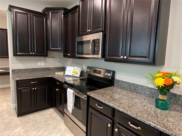 kitchen featuring light tile patterned flooring, appliances with stainless steel finishes, dark stone countertops, and dark brown cabinetry